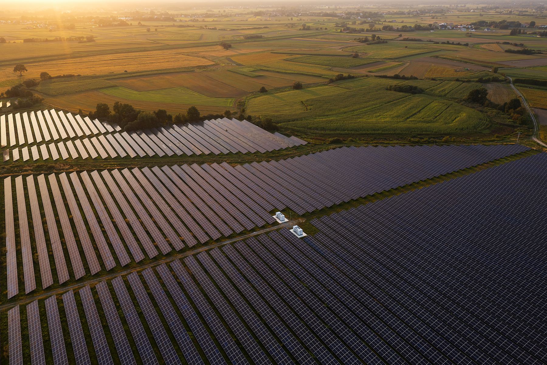 Aerial view of a large solar farm at sunrise surrounded by agricultural land